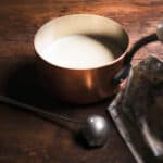 Béchamel sauce in a copper saucepan with a ladle on the side and a kitchen cloth