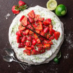 overhead view of a strawberry lime pavlova with lime, strawberries and spoons on the side