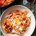 pici all'aglione in a bowl with a skillet and glass of wine on the side