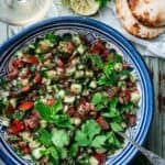 Shirazi salad in a blue bowl with flatbreads and a glass of wine on the side