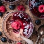 a half eaten chocolate panna cotta with berry compote in a glass with other panna cotta on the side