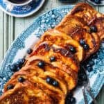 brioche french toast in a vintage blue serving plate with blueberries and drizzled with maple syrup