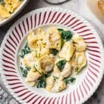 cheese tortellini with wine sauce, topped with cheese and chives in a red and white pasta bowl.