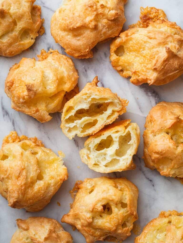 gougères on a marble surface with one gougère cut in half.