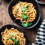 two black bowls of peanut noodles with chili crisp and cilantro on the side