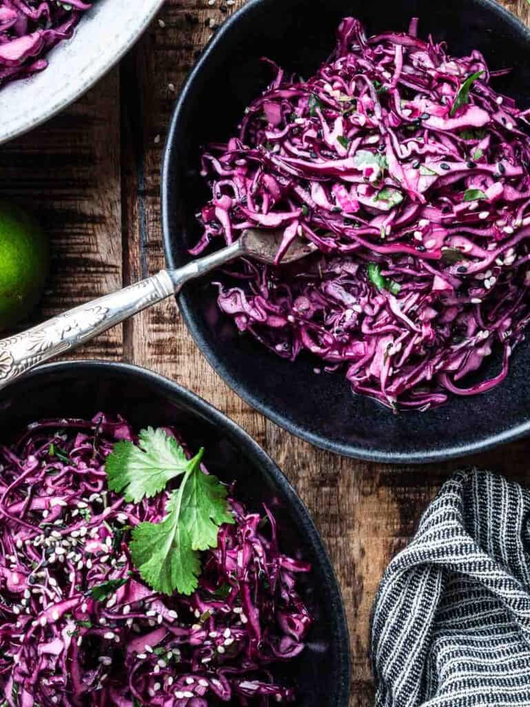 two black bowls of red cabbage slaw with a fork.