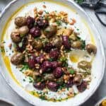 whipped ricotta dip topped with roasted olives and pine nuts in a white bowl