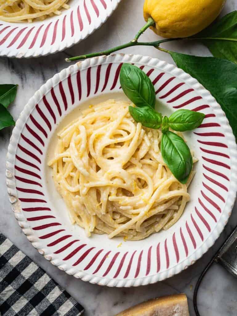lemon pasta with basil in a stripped red and white bowl.