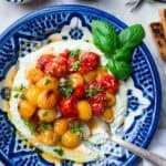 whipped feta dip with roasted cherry tomatoes on top in a blue bowl.