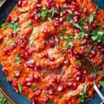 muhammara with fresh pomegranate topped with parsley in blue bowl.