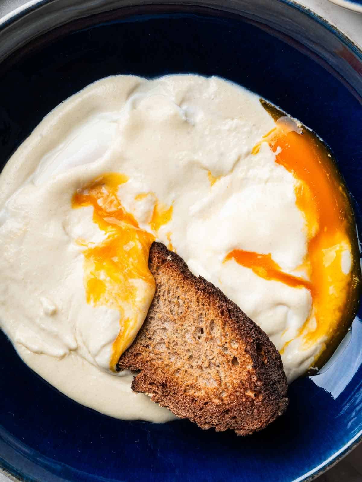 runny poached eggs in brie cheese sauce with a slice of toasted sourdough bread.