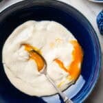 runny poached eggs in brie cheese sauce in a blue bowl.