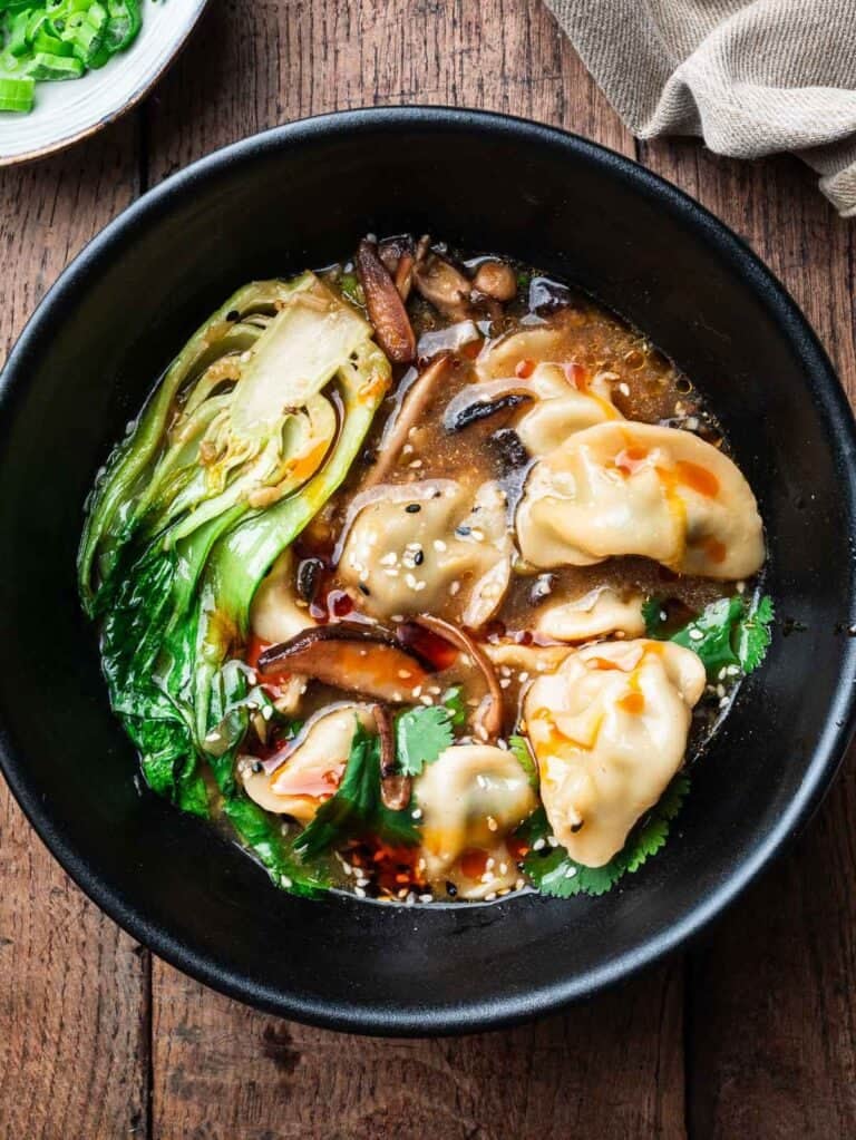 vegetarian dumpling soup with mushrooms and bok choy in a black bowl.