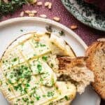 garlic baked brie with a torn piece of sourdough bread, topped with parsley.