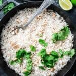 basmati coconut rice in a black cast iron braiser with a spoon topped with cilantro.