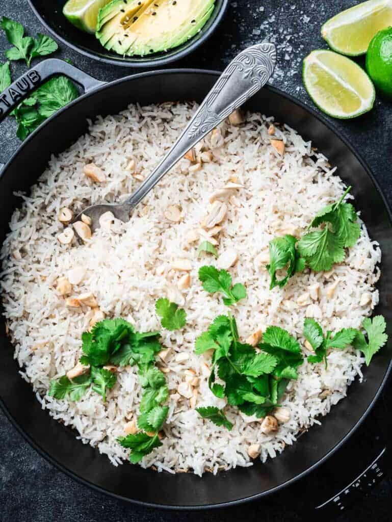 basmati coconut rice in a black cast iron braiser with a spoon topped with cilantro.