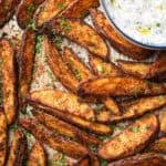 roasted Mediterranean potato wedges on a tray topped with parsley with a yogurt dip on the side.