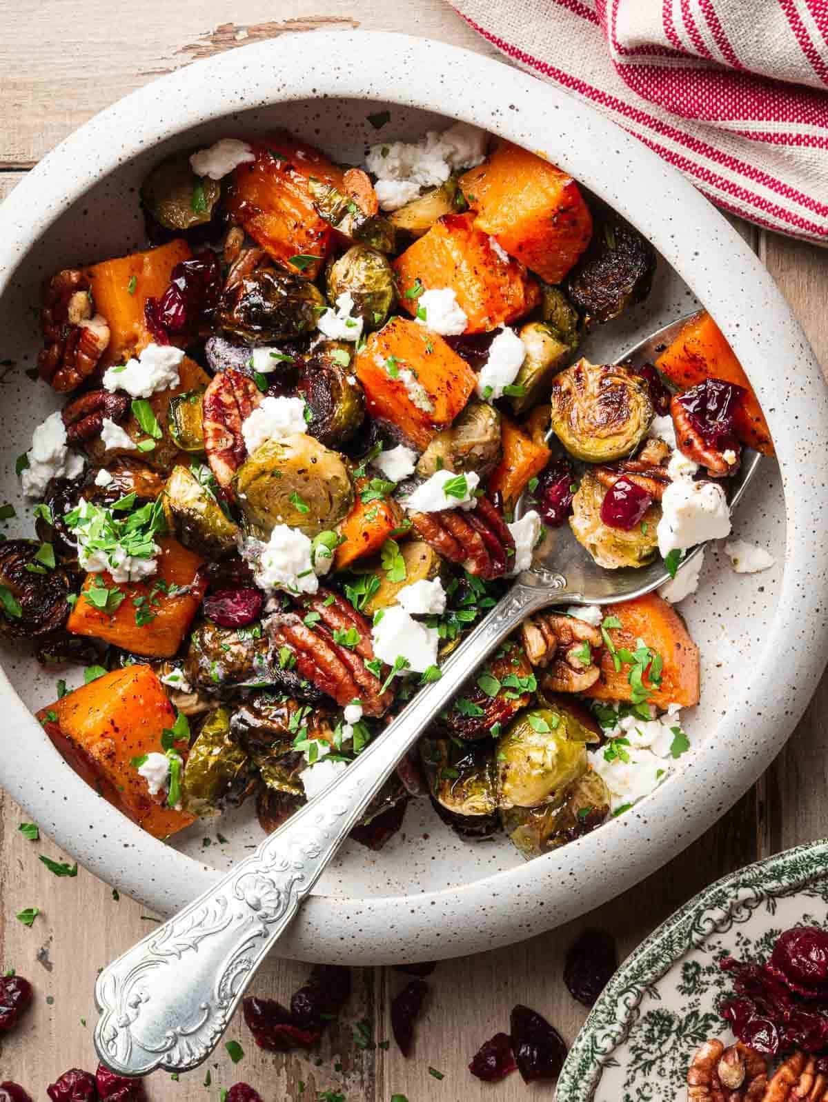 a bowl with roasted Brussels sprouts, sweet potatoes, pecans, cranberries and goat cheese.