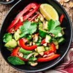 bell pepper cucumber salad in a black bowl with a stripped kitchen cloth.