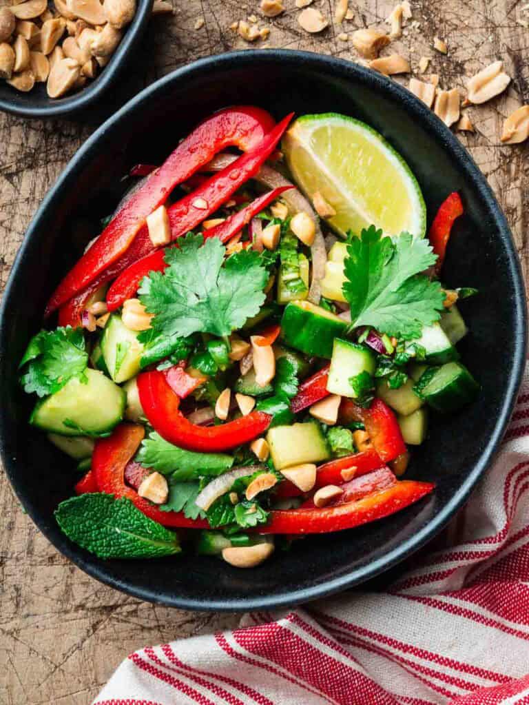 bell pepper cucumber salad in a black bowl with a stripped kitchen cloth.
