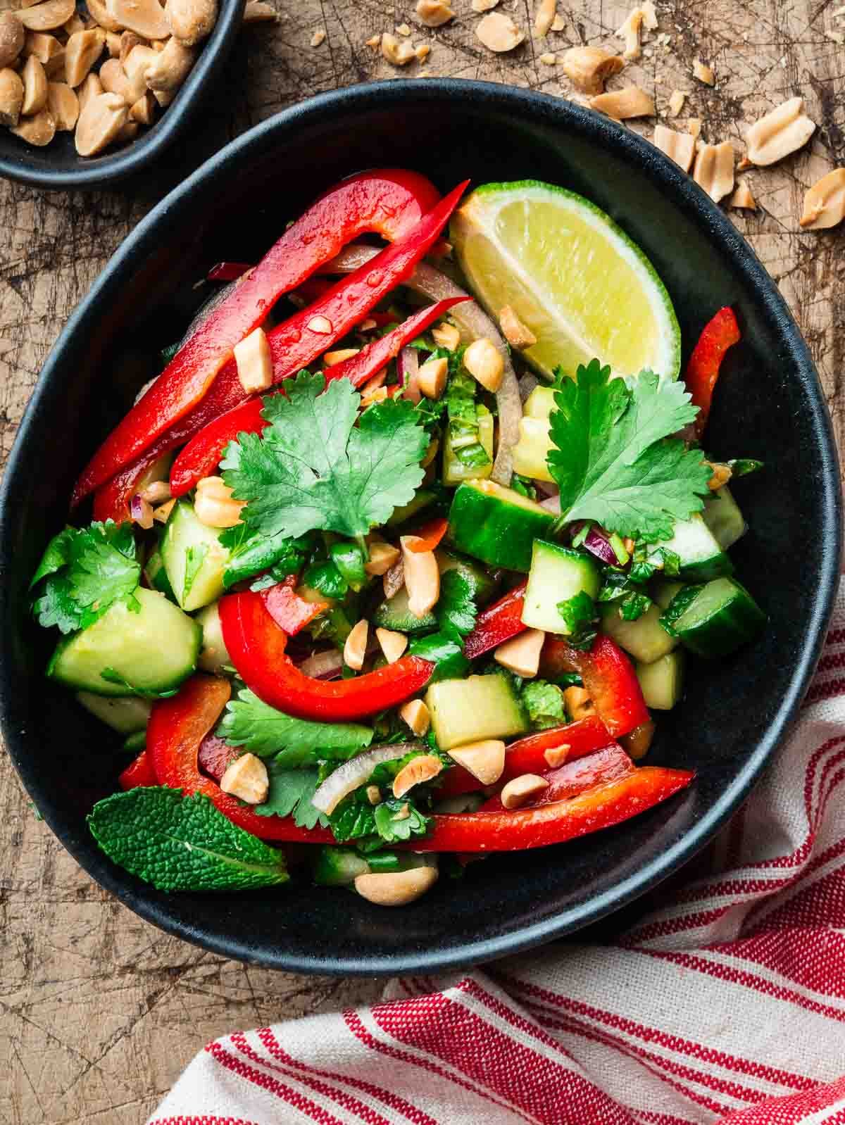 bell pepper cucumber salad in a black bowl with a stripped kitchen cloth.