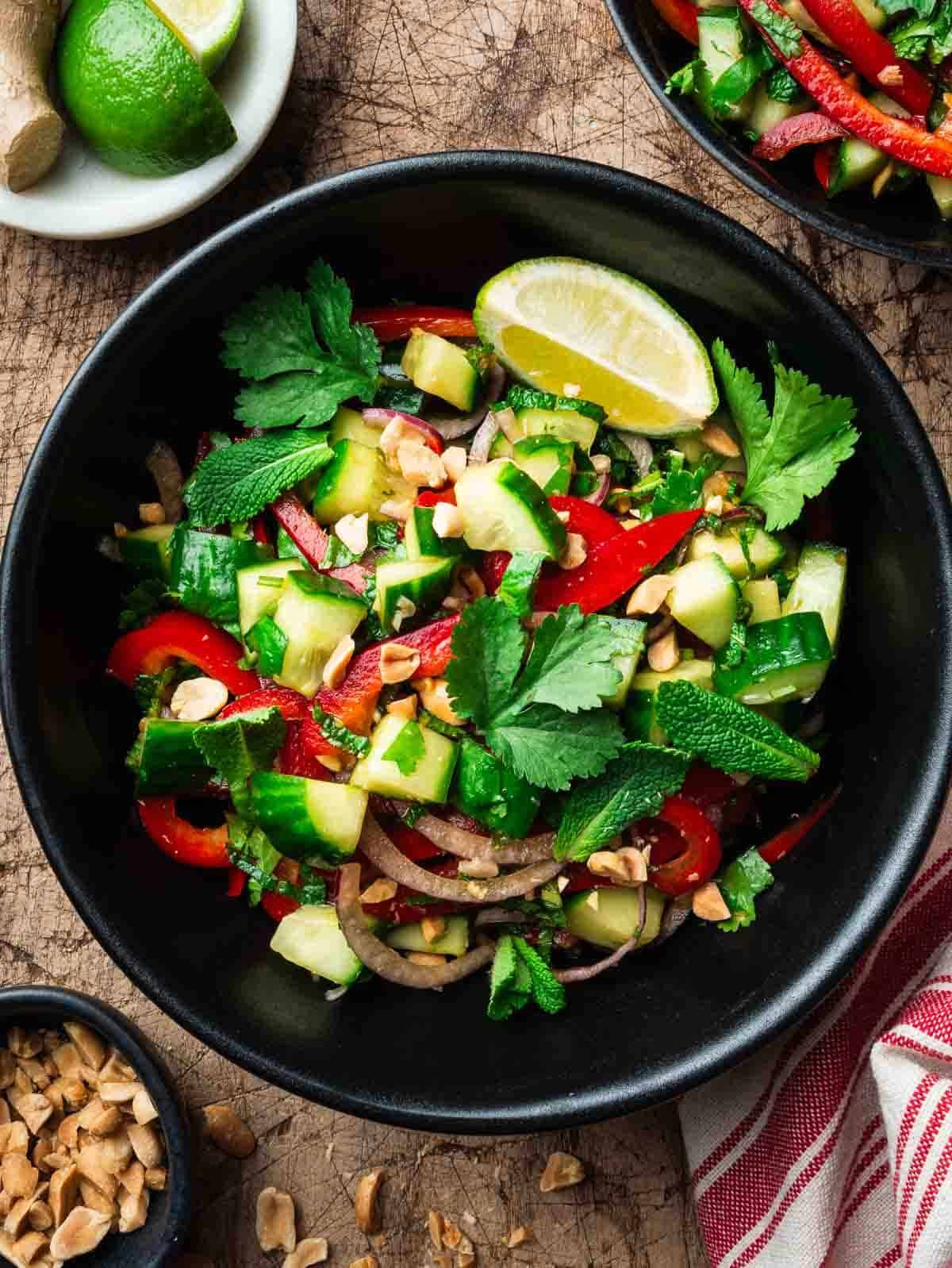 bell pepper cucumber salad in a black bowl with chopped peanuts on the side.