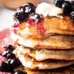 stack of blueberry lemon pancakes topped with blueberry compote, maple syrup and butter.