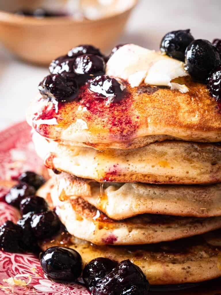stack of blueberry lemon pancakes topped with blueberry compote, maple syrup and butter.