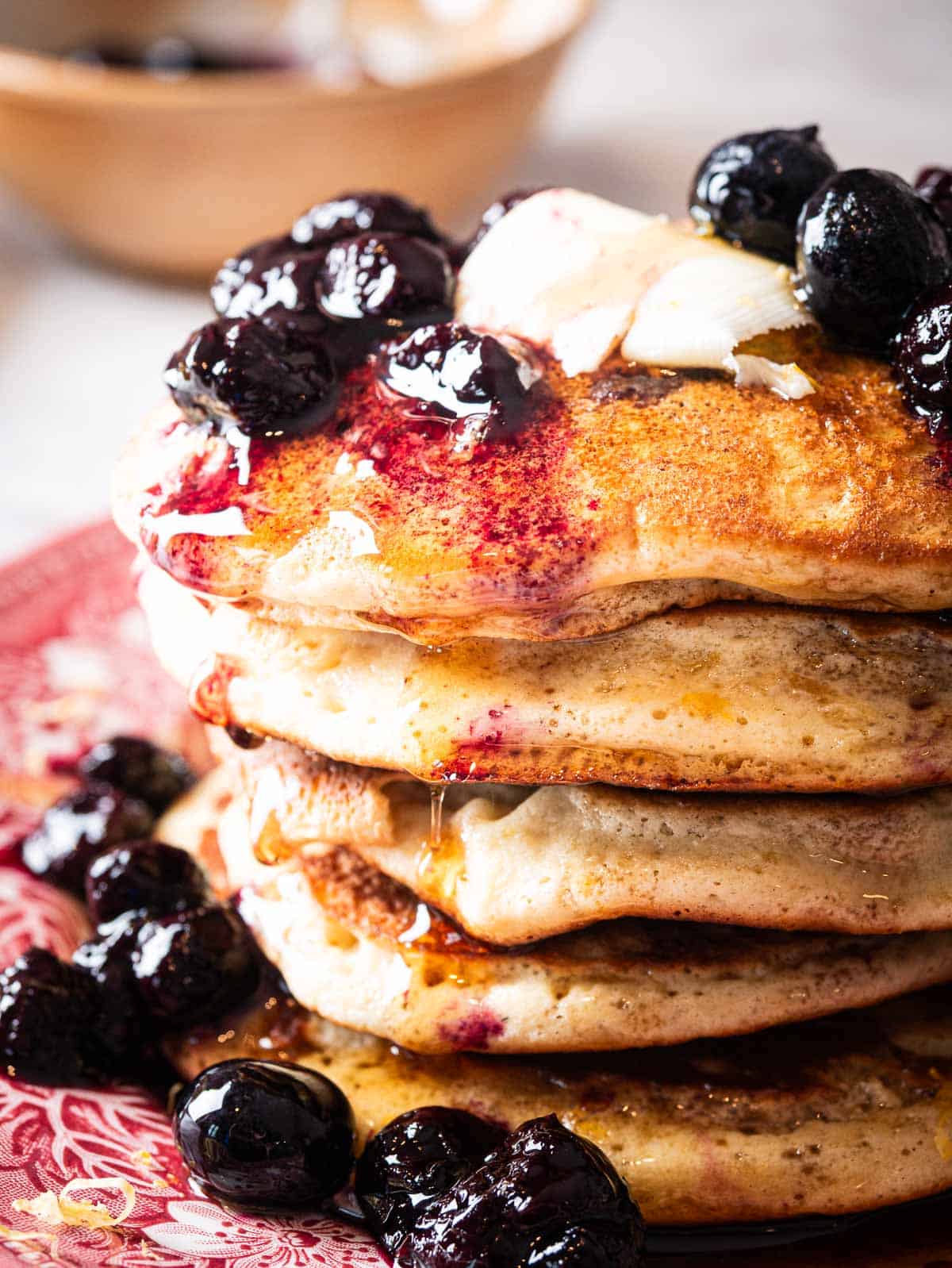 a stack of blueberry lemon pancakes topped with blueberry compote and maple syrup.