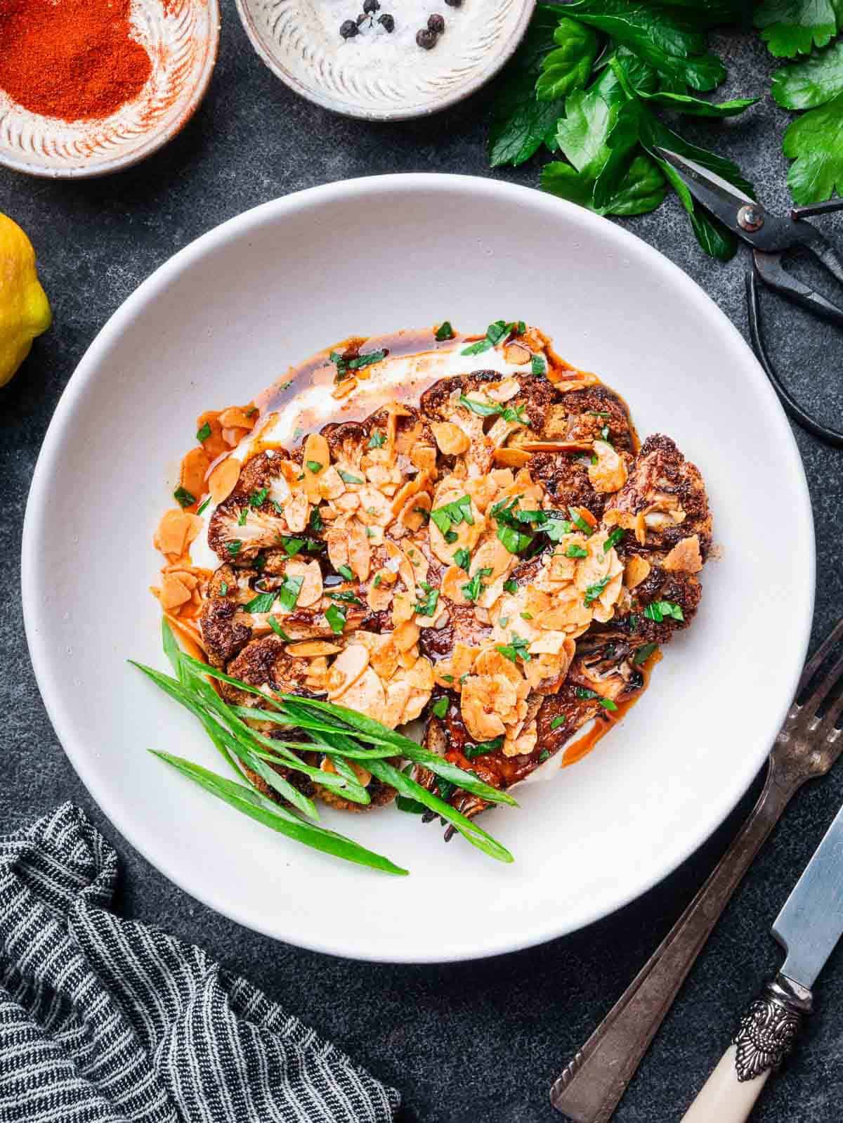 roasted cauliflower steaks on yogurt sauce with almond paprika butter in a bowl with a fork on the side.