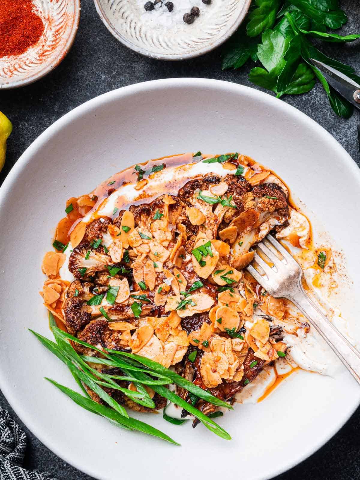 roasted cauliflower steaks on tahini yogurt sauce with almond paprika butter with a fork.