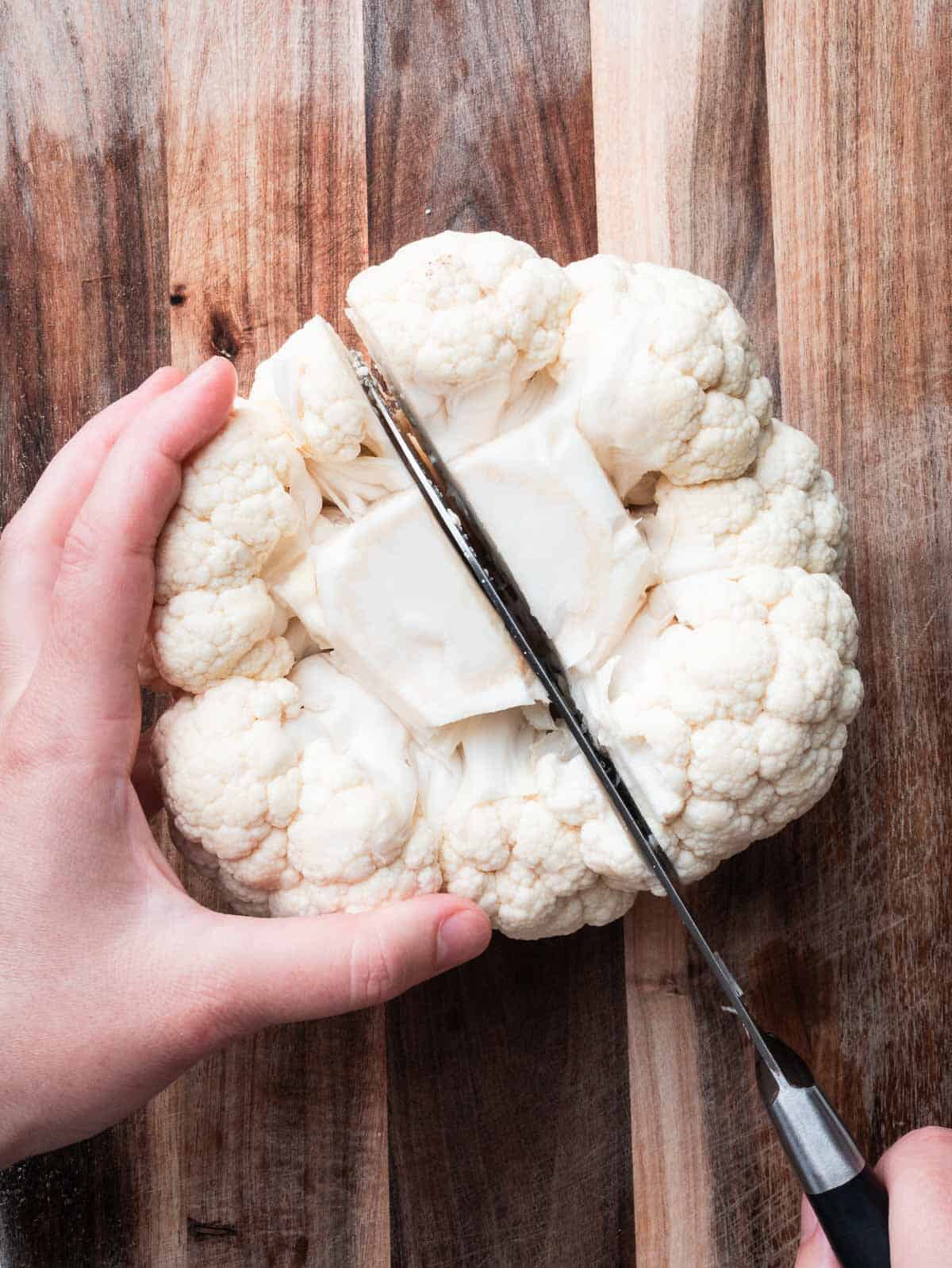 a cauliflower head cut in half with a kitchen knife.