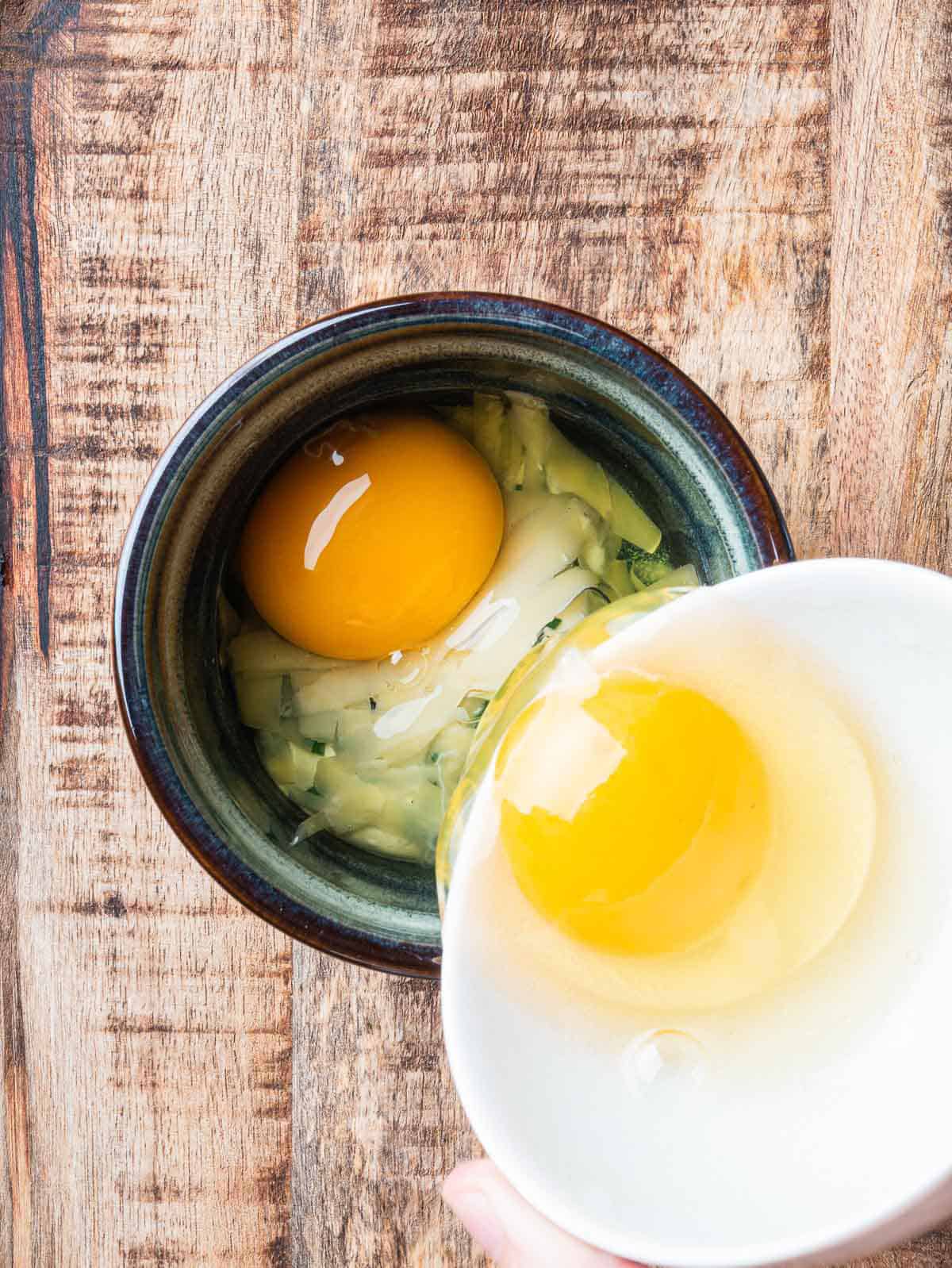 eggs being poured on top of crème fraîche and grated Comté in a ramekin.