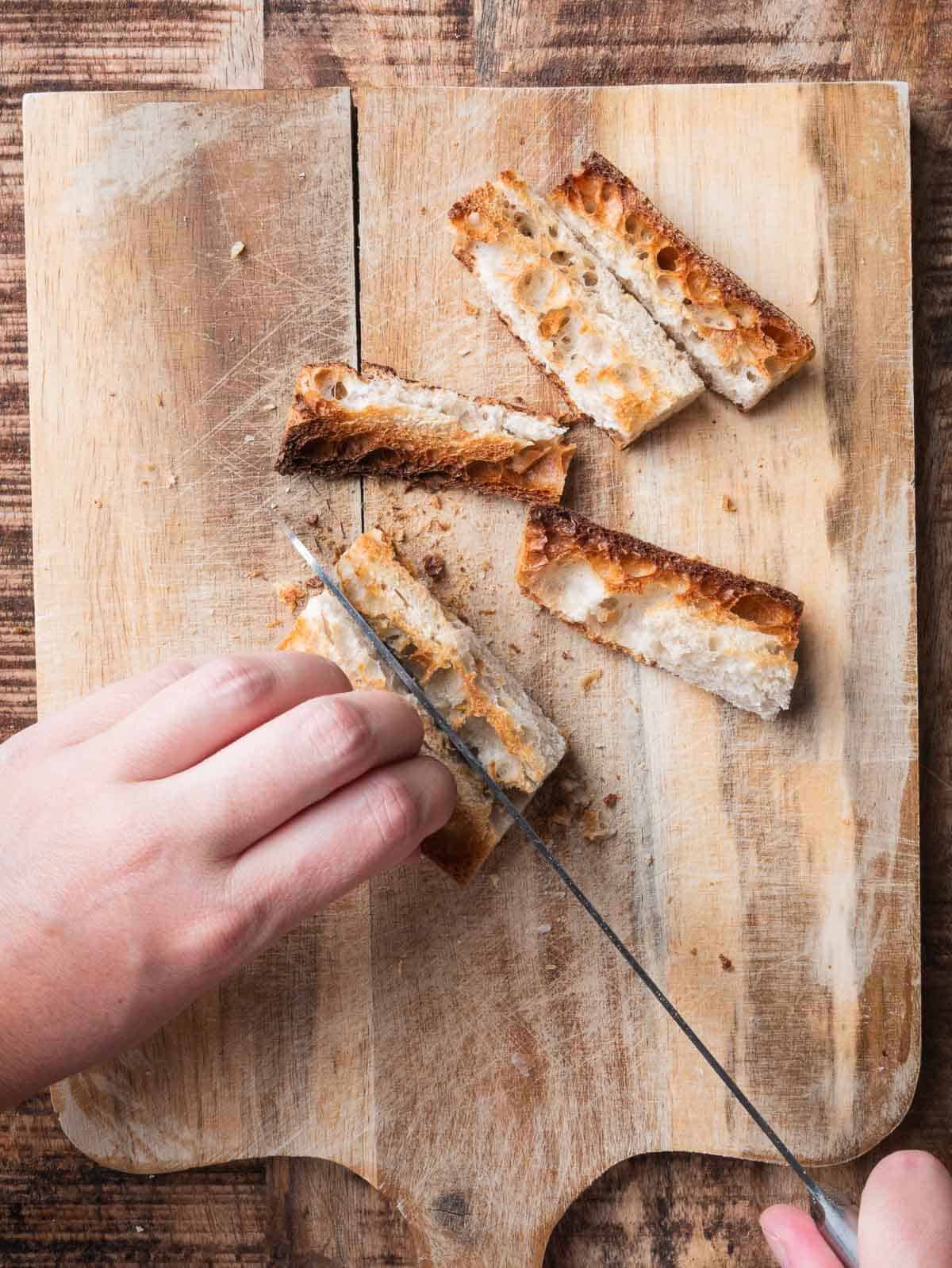 hands cutting toasted baguette into finger shape.