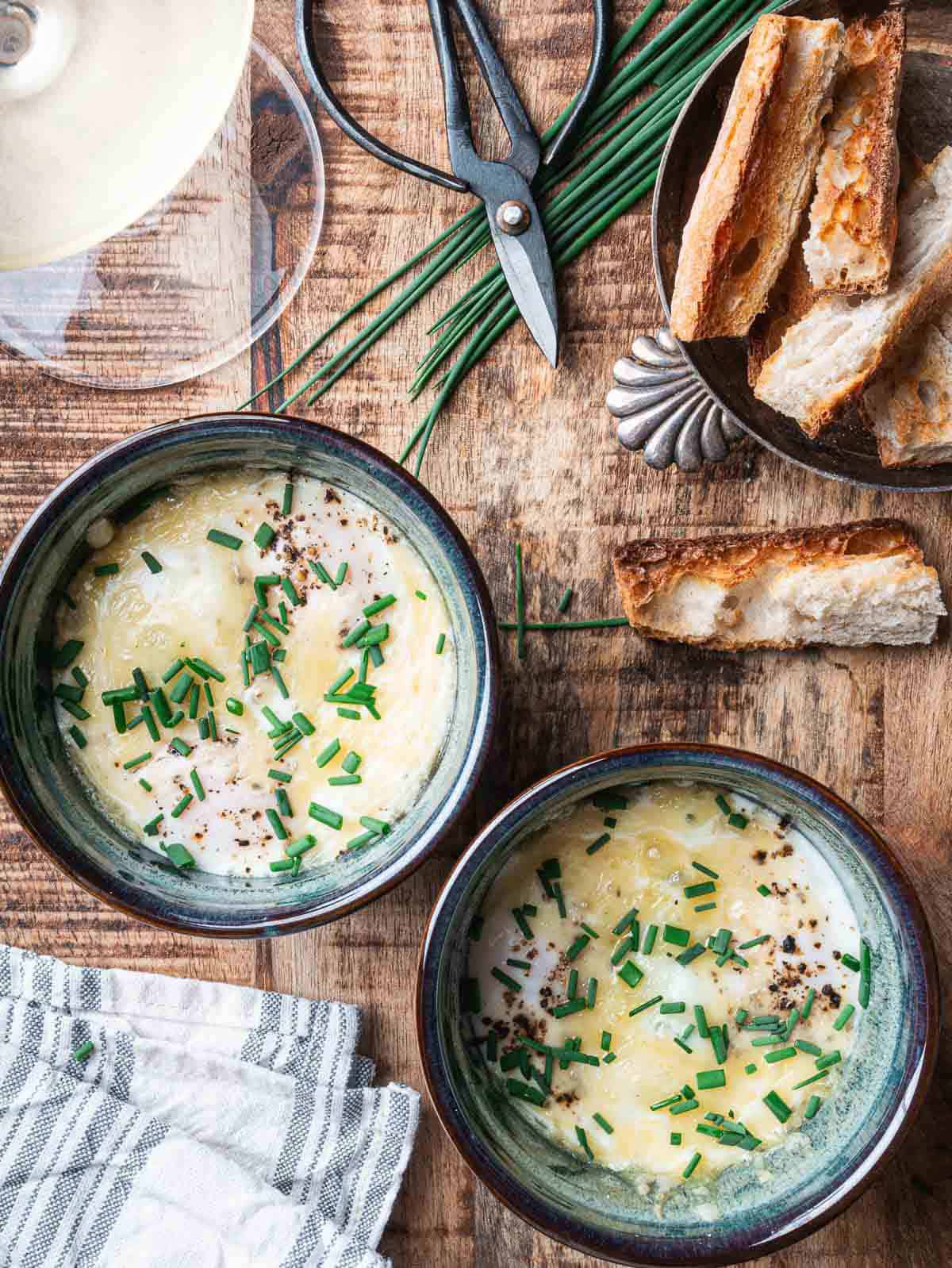 two baked eggs in blue ramekins with a glass of white wine on the side.