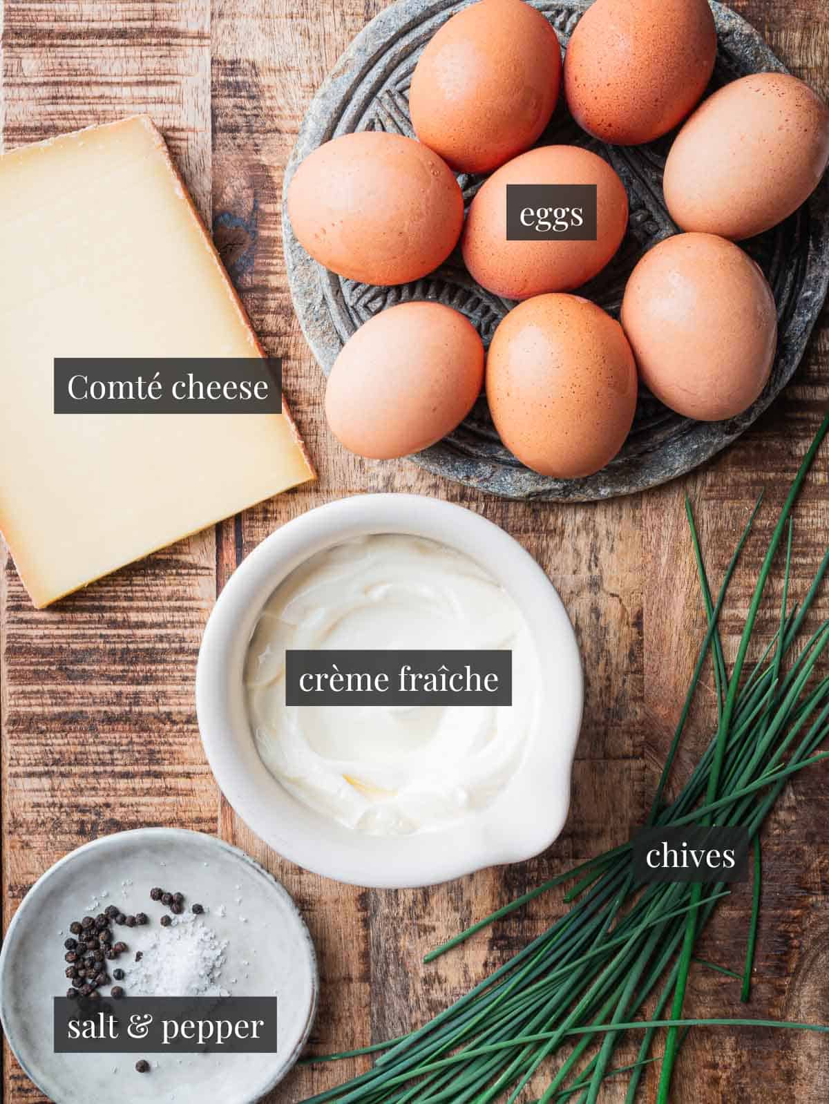 eggs, Comté cheese, crème fraîche, chives, salt and pepper on a wooden background.