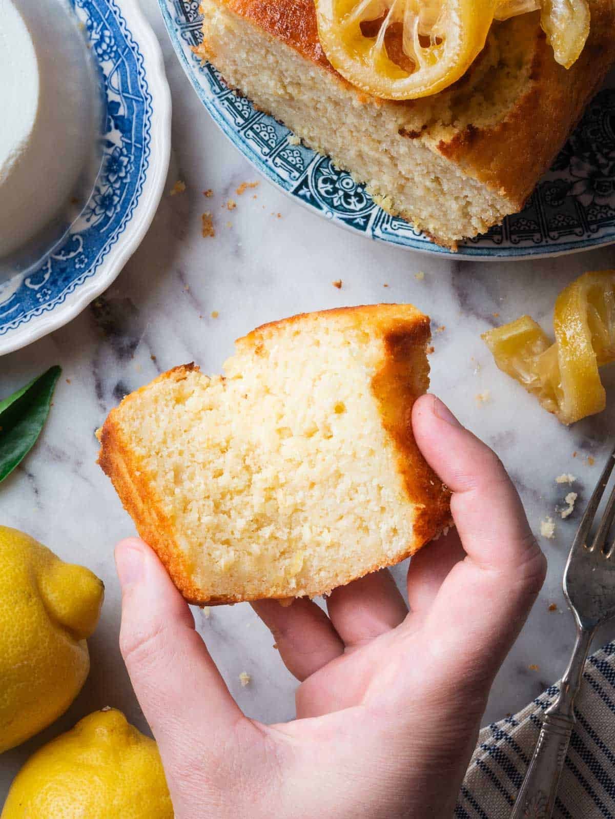 a hand holding a slice of lemon ricotta pound cake.