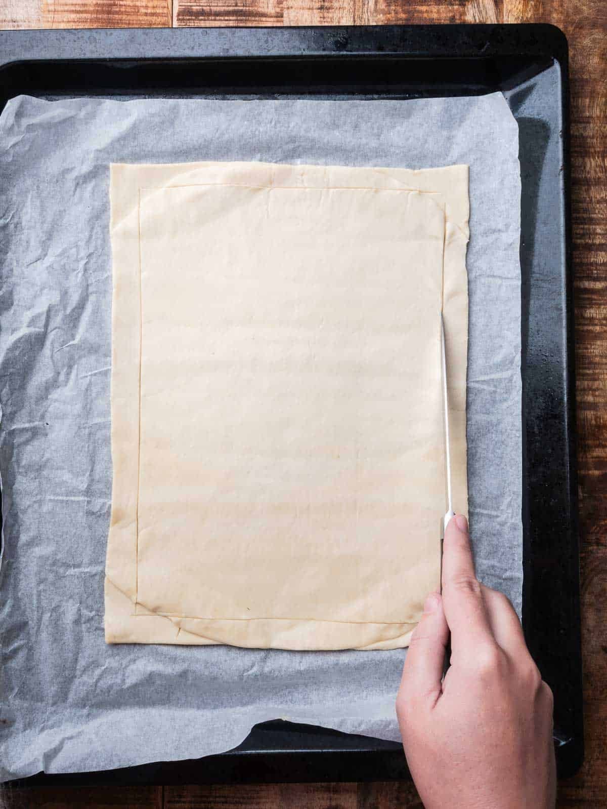 hand scoring puff pastry with a knife.