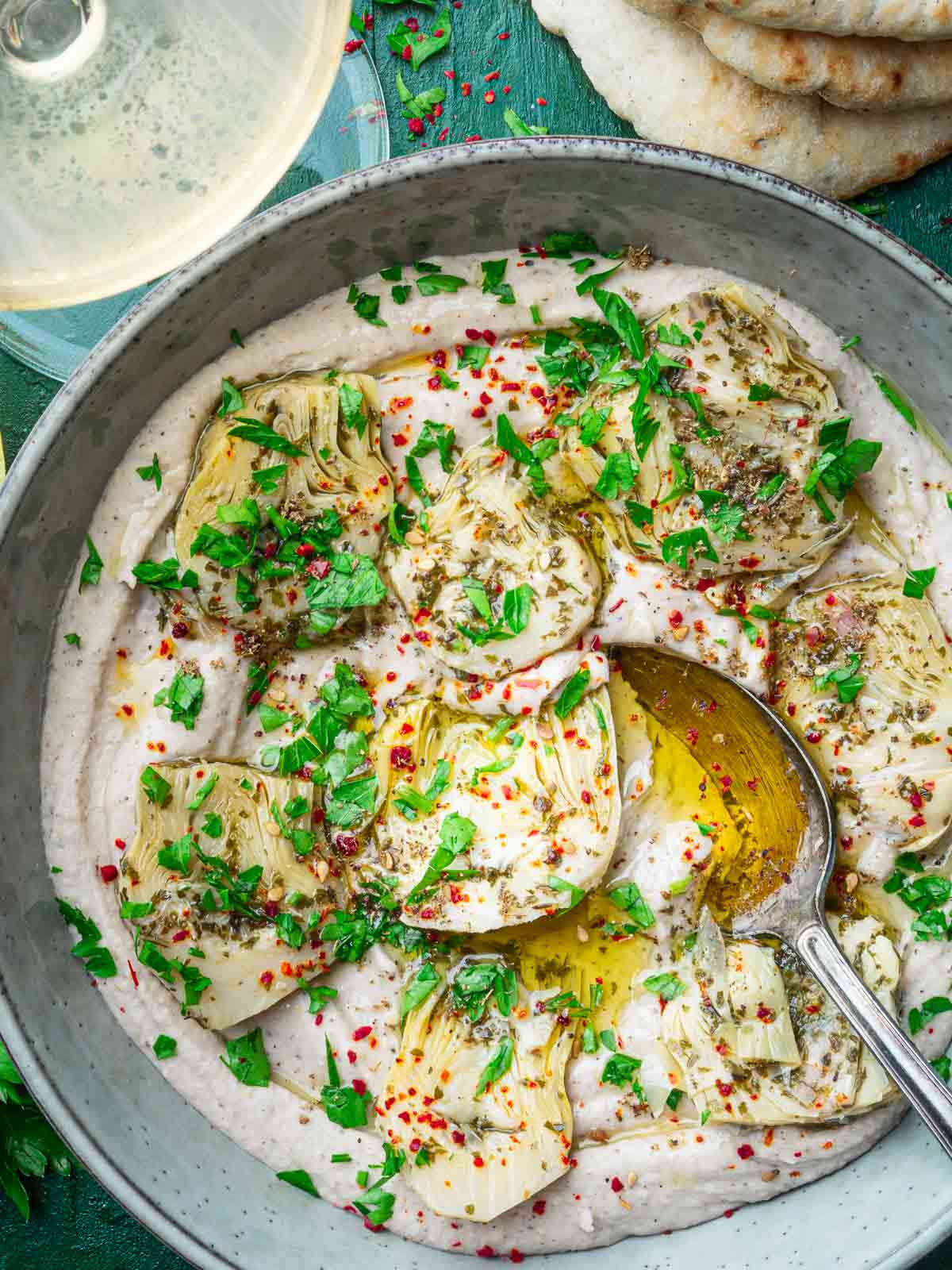 creamy white bean dip topped with artichoke hearts, parsley, olive oil and chili flakes with a spoon.