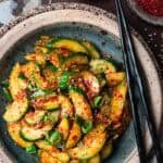 spicy Korean cucumber salad in a blue plate with black chopsticks.