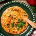 Feta and red pepper dip in a green plate with a wooden spoon.