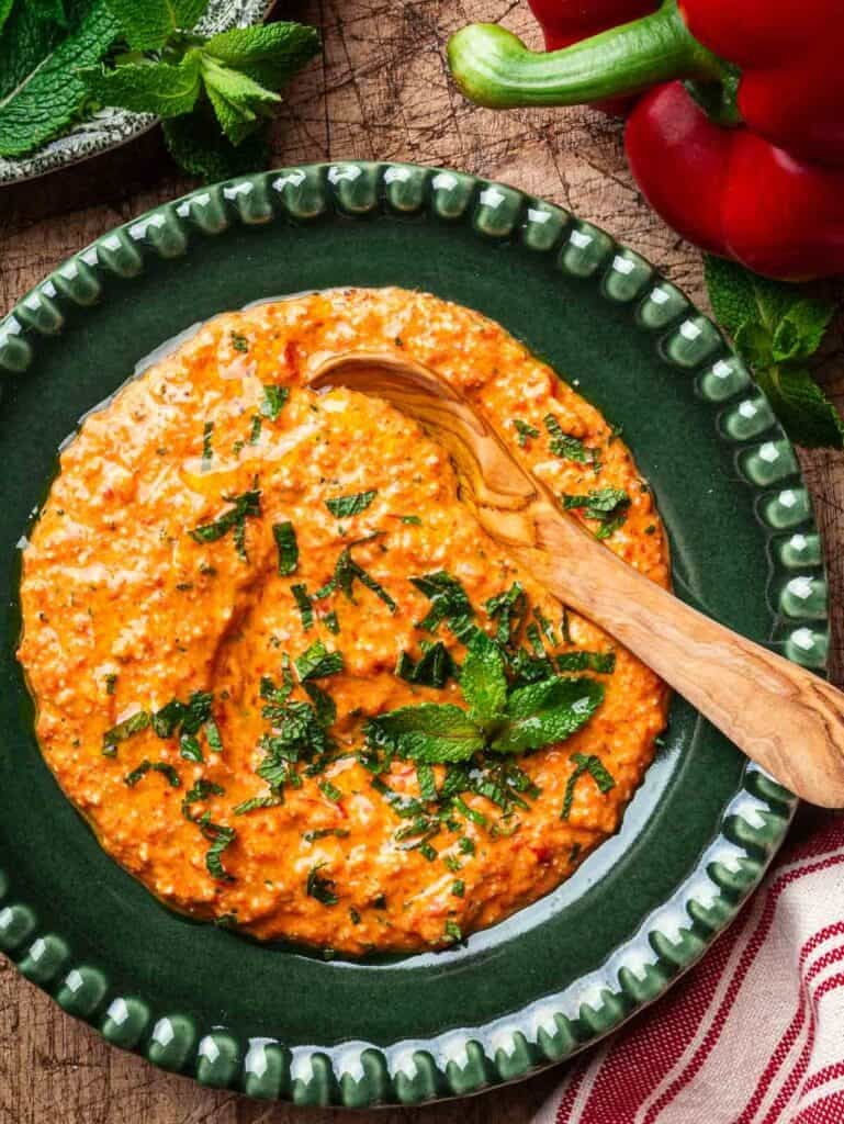 Feta and red pepper dip in a green plate with a wooden spoon.