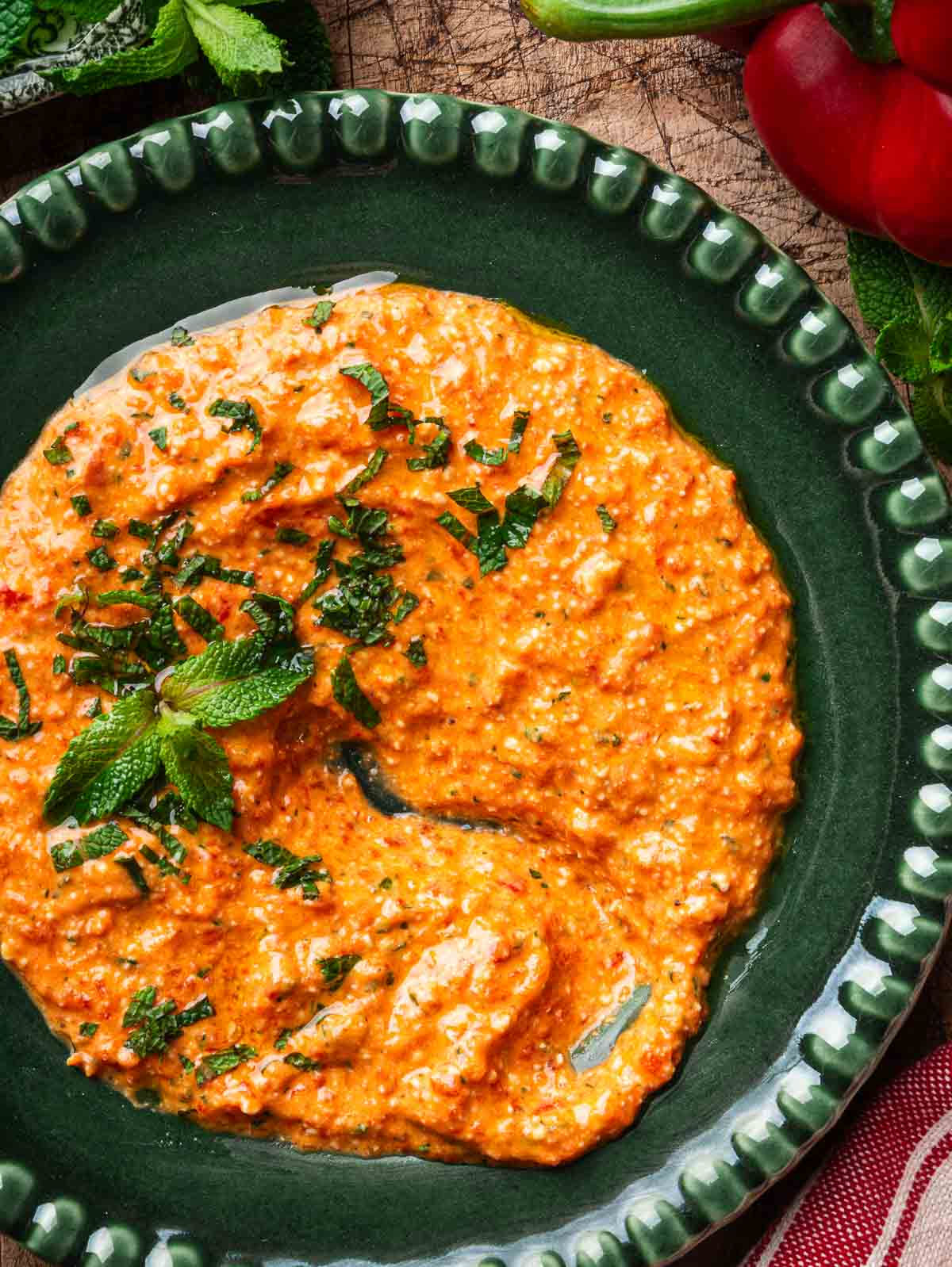 Creamy feta and roasted red pepper dip on a green plate, with a portion scooped out.