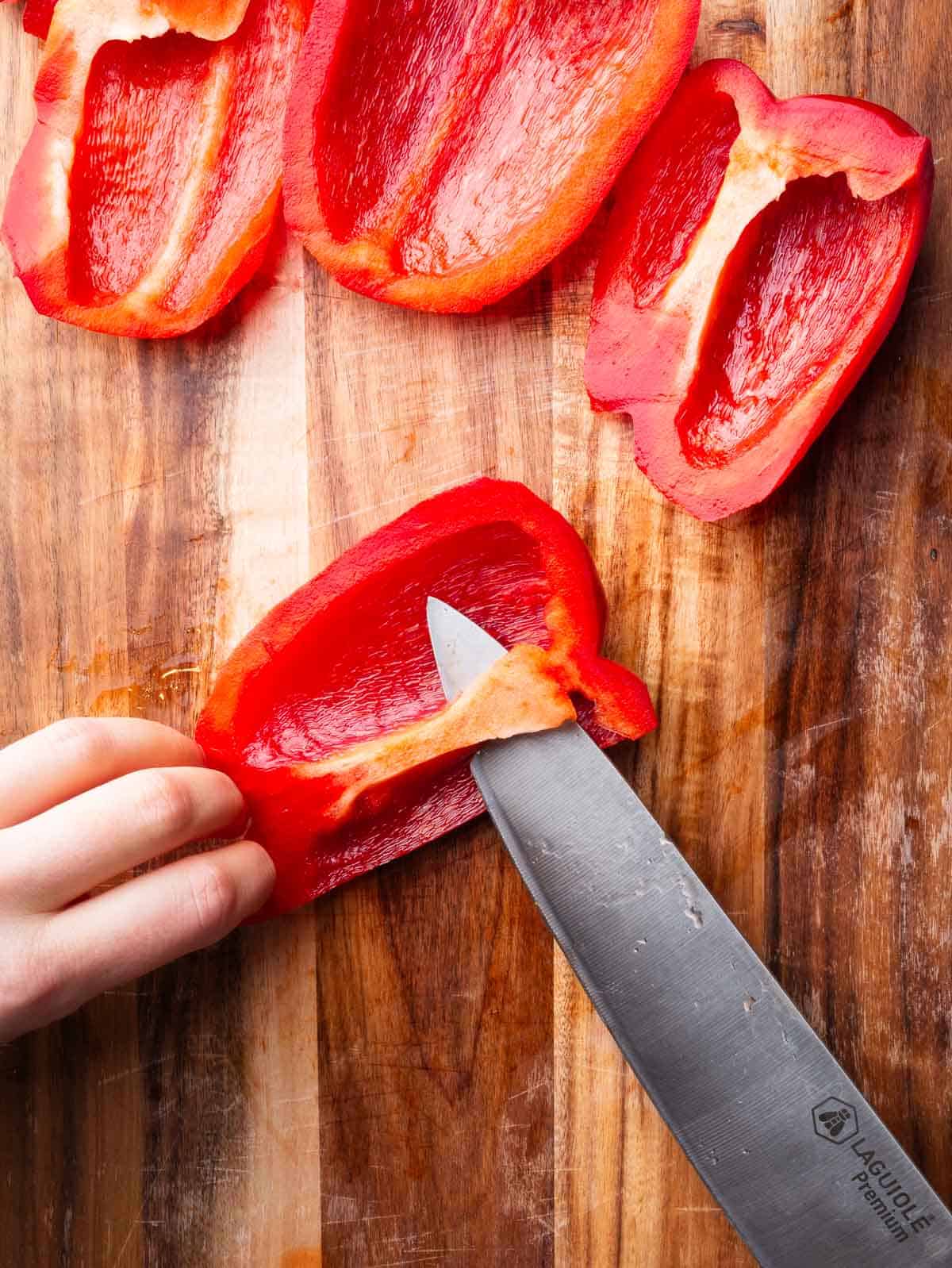 Hands removing the white part of a red bell pepper with a kitchen knife.