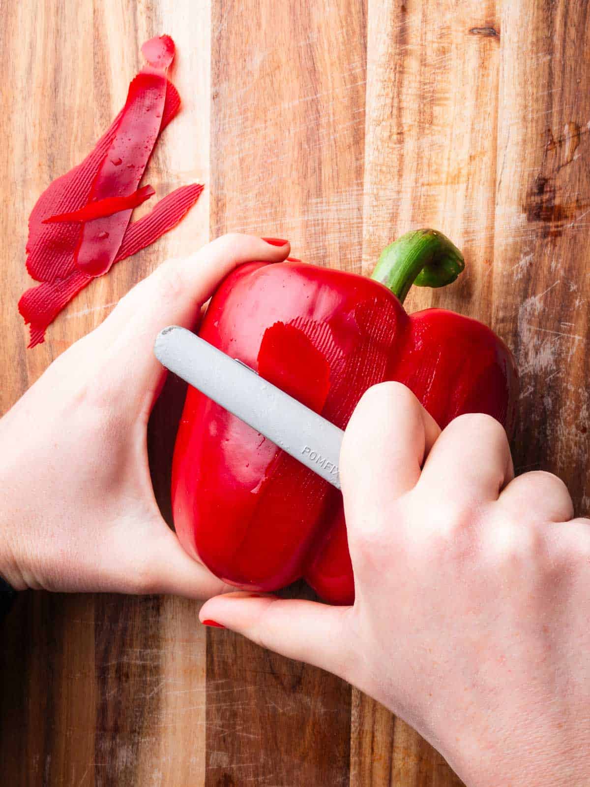 Hands peeling a red bell pepper with a vegetable 