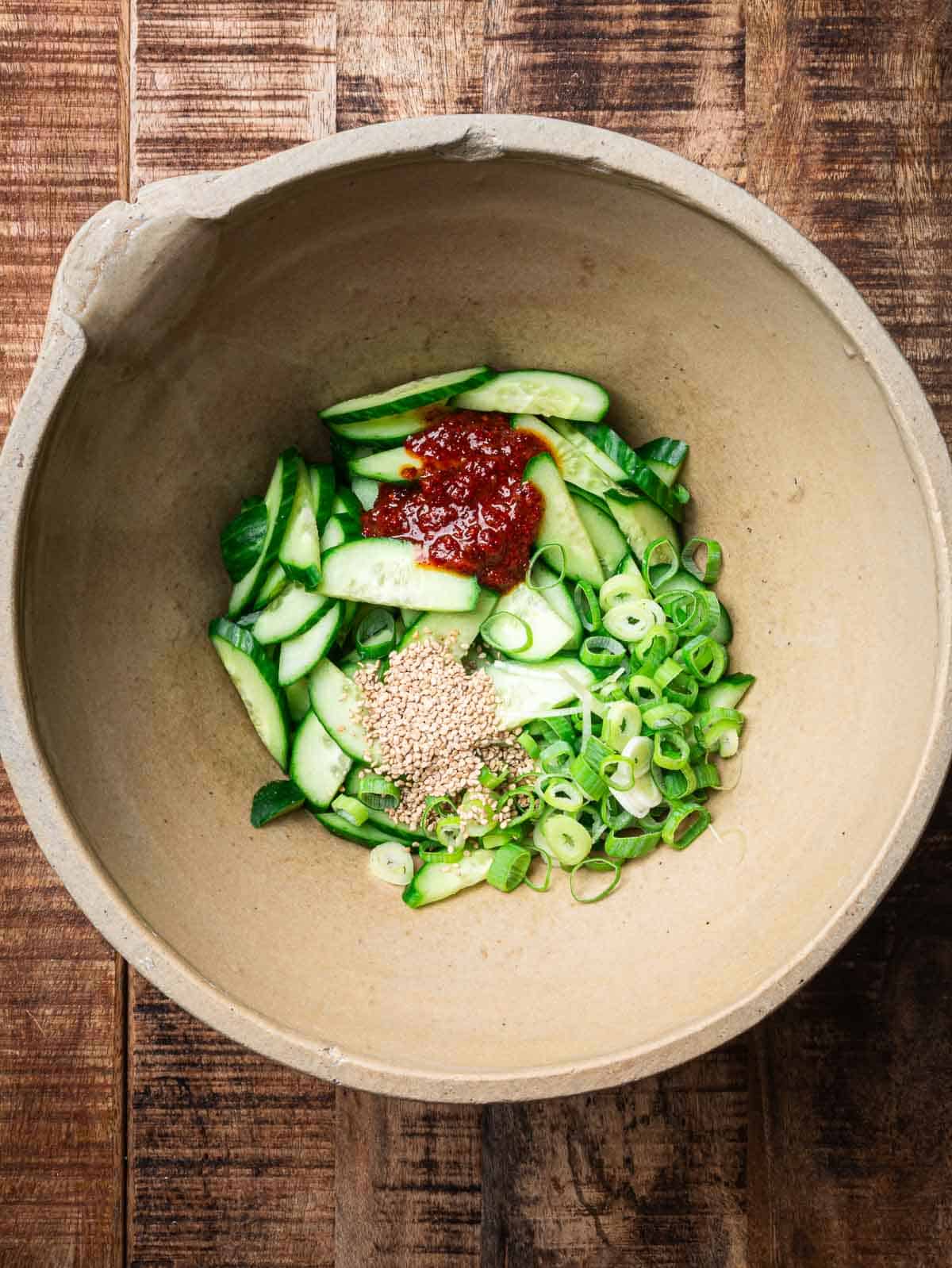 sliced cucumbers, chopped scallions, gochugaru dressing, sesame seeds in a mixing bowl. 