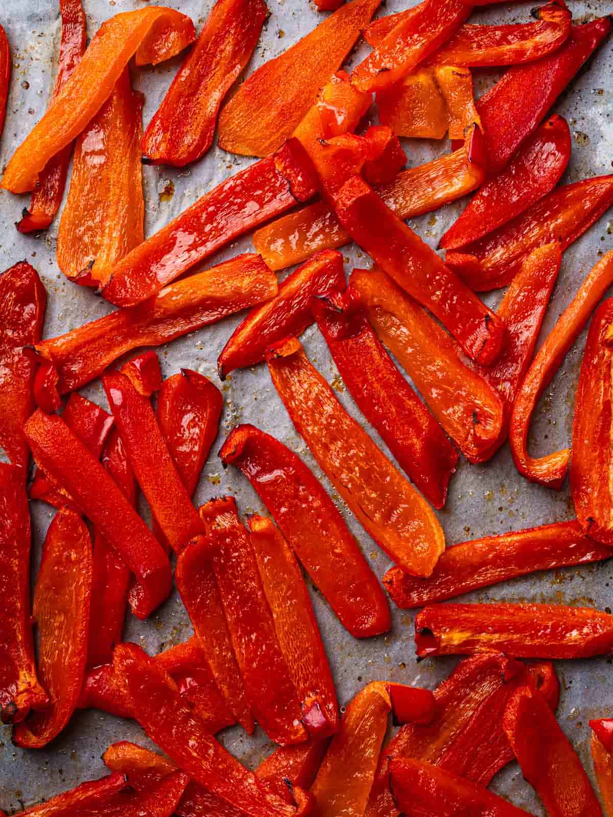 Oven roasted red pepper strips on a parchment lined tray.