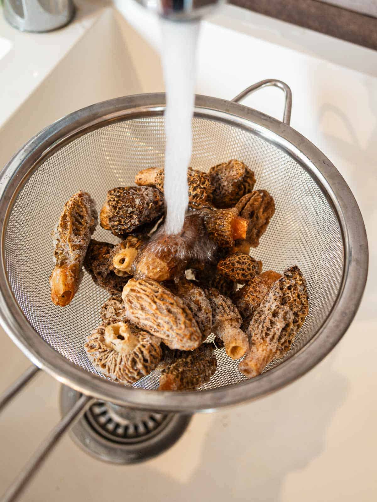 frozen morels in a fine mesh strainer rinser under cold water.