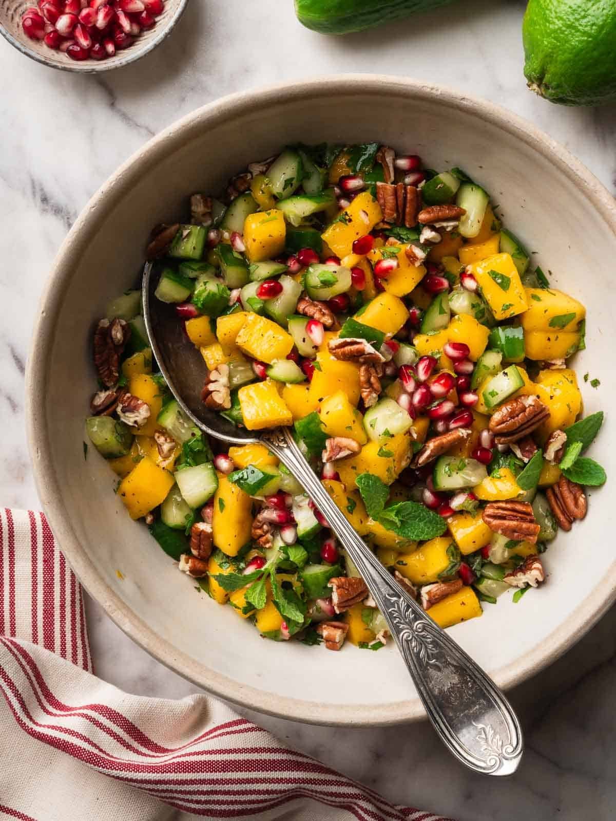 Cucumber, mango, pecan and pomegranate salad with a spoon. and a kitchen cloth.
