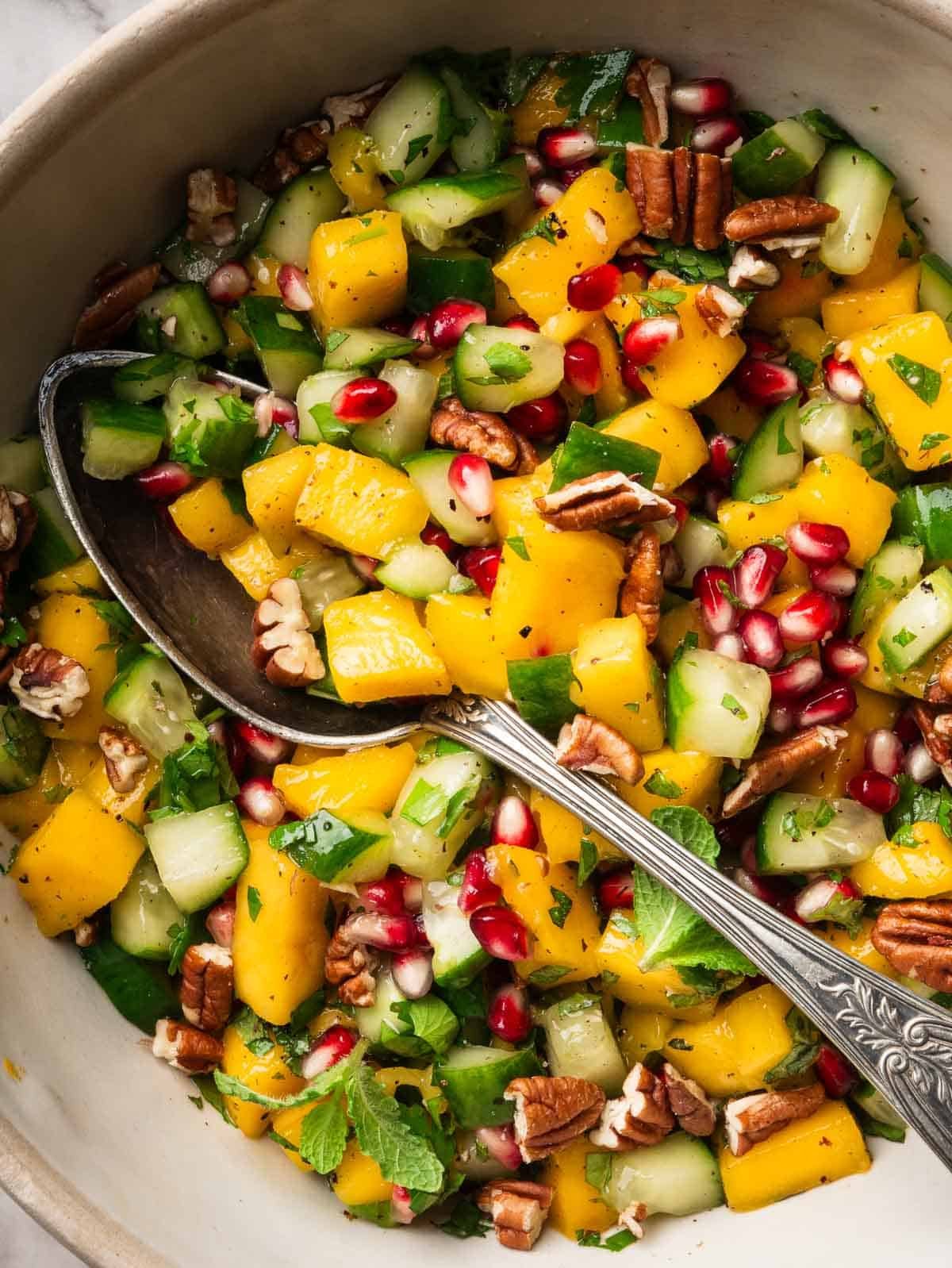 Cucumber, mango, pecan and pomegranate salad with a spoon.